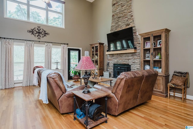 living room with a towering ceiling, a fireplace, ceiling fan, and light wood-type flooring