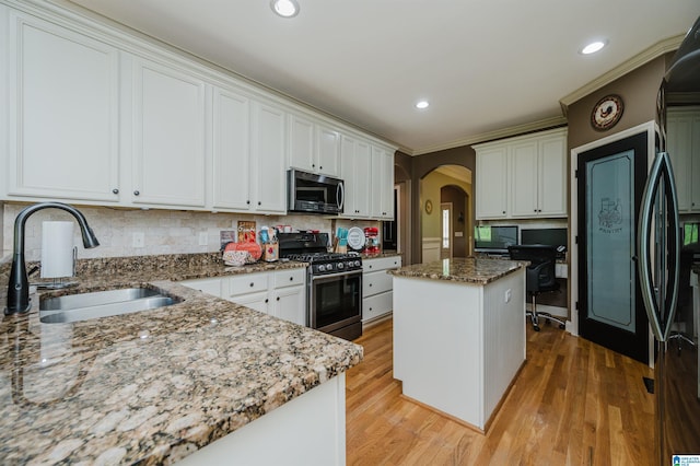 kitchen featuring sink, appliances with stainless steel finishes, light stone counters, white cabinets, and a kitchen island