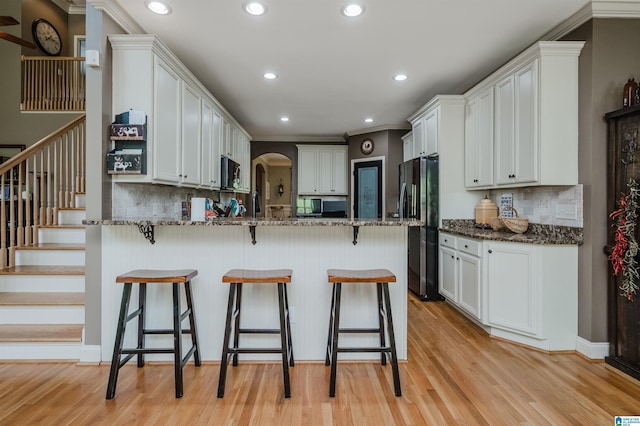 kitchen featuring light hardwood / wood-style flooring, dark stone countertops, backsplash, white cabinets, and black fridge