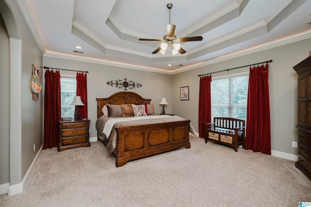 carpeted bedroom with multiple windows, ornamental molding, ceiling fan, and a tray ceiling