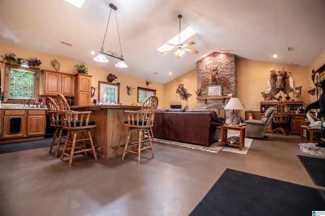 kitchen featuring lofted ceiling, a kitchen breakfast bar, a stone fireplace, ceiling fan, and kitchen peninsula