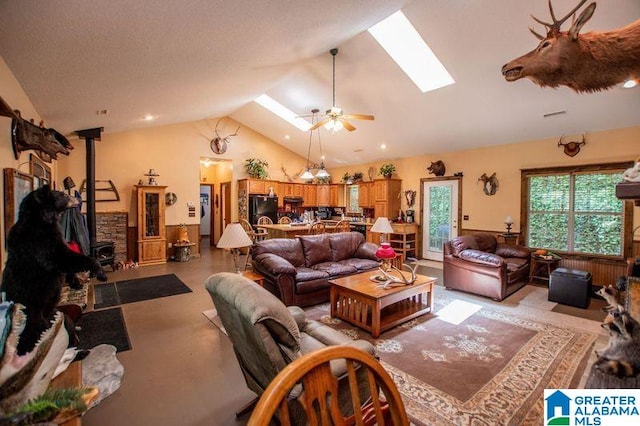 living room with a wood stove, ceiling fan, and lofted ceiling with skylight