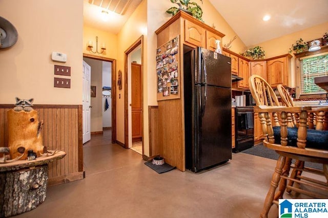 kitchen with stove, concrete flooring, vaulted ceiling, wooden walls, and black refrigerator