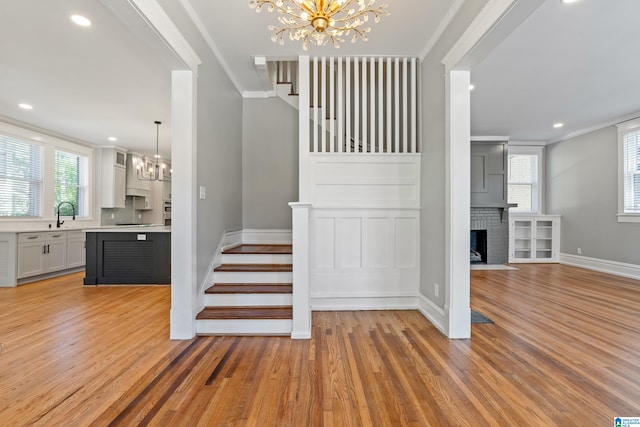 staircase with sink, a fireplace, crown molding, hardwood / wood-style flooring, and an inviting chandelier