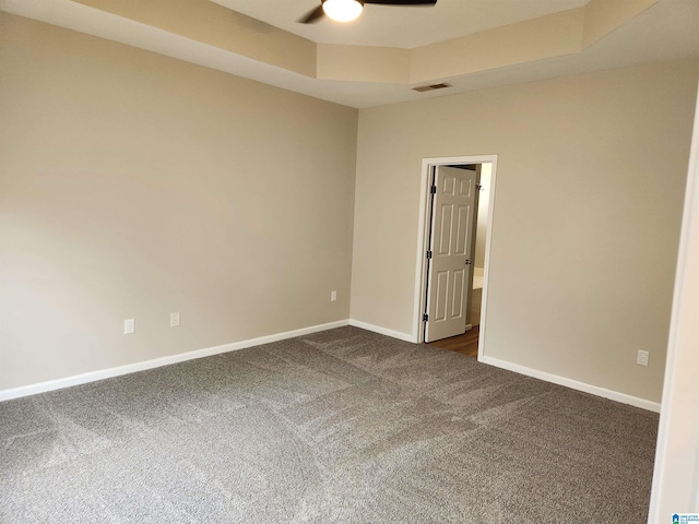 unfurnished room featuring baseboards, visible vents, a raised ceiling, ceiling fan, and dark colored carpet