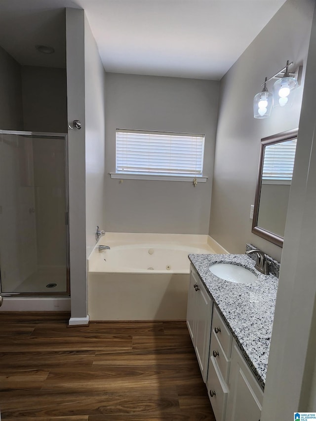 bathroom with a stall shower, a tub with jets, wood finished floors, and vanity