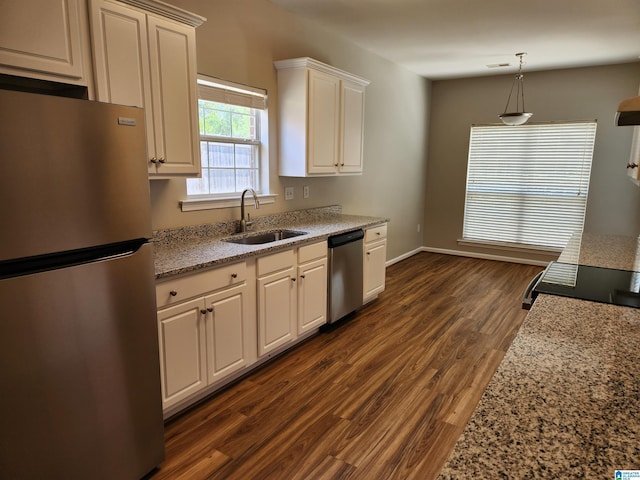 kitchen with pendant lighting, appliances with stainless steel finishes, dark wood-type flooring, a sink, and light stone countertops