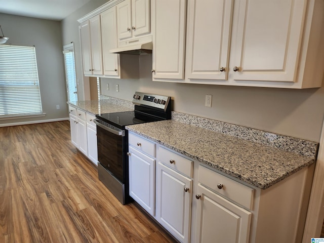 kitchen with light hardwood / wood-style floors, light stone countertops, white cabinetry, electric range, and wall chimney exhaust hood