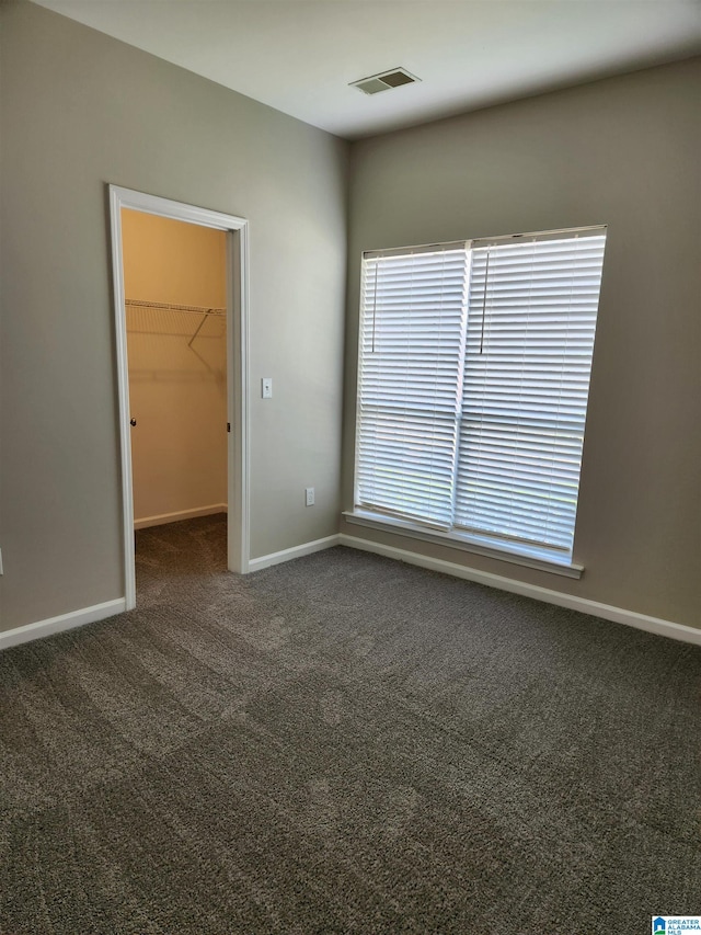 unfurnished bedroom featuring dark carpet, a closet, and a spacious closet