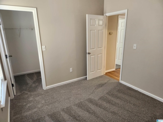 unfurnished bedroom with carpet floors, a walk in closet, a closet, and baseboards