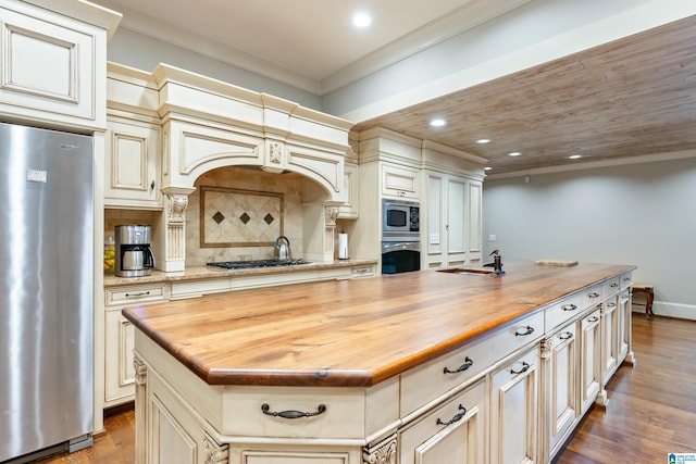 kitchen featuring a kitchen island with sink, wooden counters, ornamental molding, decorative light fixtures, and light hardwood / wood-style floors