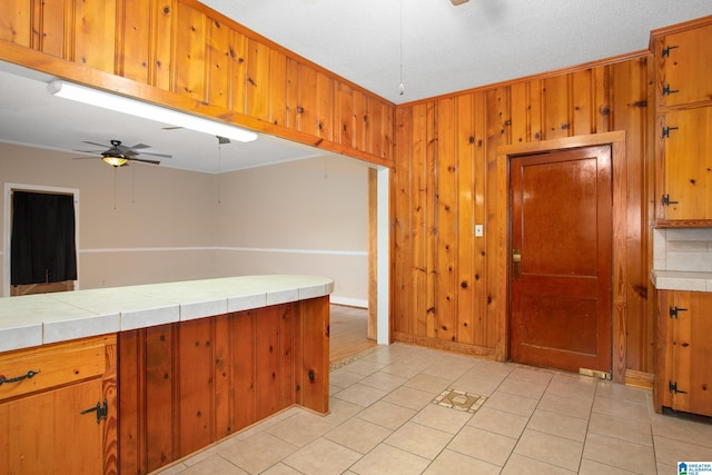 kitchen with ceiling fan, tile countertops, a textured ceiling, wooden walls, and light tile patterned floors