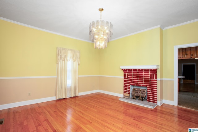 unfurnished living room featuring hardwood / wood-style floors, ornamental molding, a brick fireplace, and an inviting chandelier