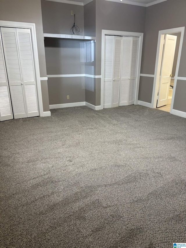 unfurnished bedroom with carpet floors, crown molding, and two closets