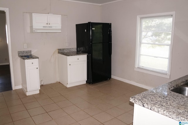 kitchen with white cabinetry, black refrigerator, light stone counters, and light tile patterned floors