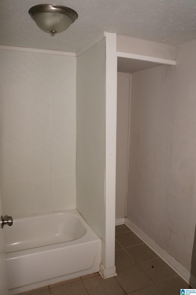 bathroom with a textured ceiling, a bathtub, and tile patterned flooring