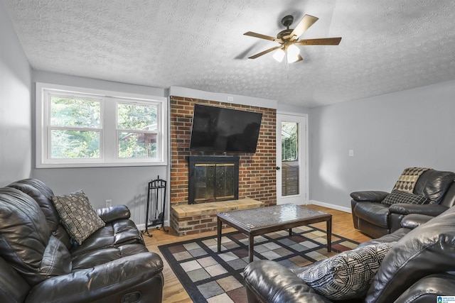 living room with ceiling fan, a textured ceiling, a fireplace, and light hardwood / wood-style flooring