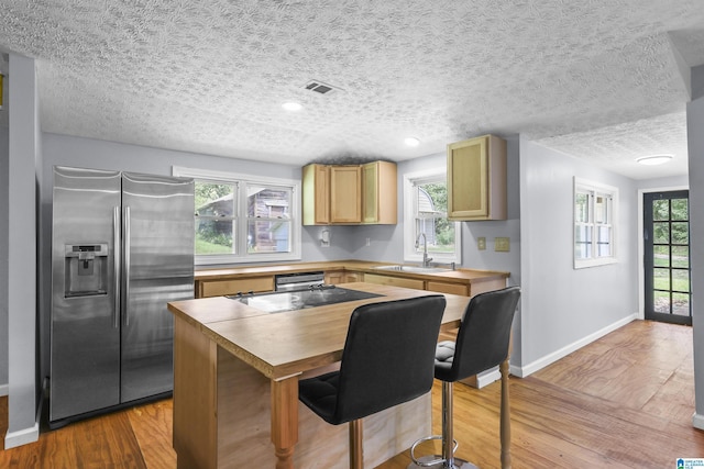 kitchen with sink, black cooktop, stainless steel fridge with ice dispenser, light hardwood / wood-style flooring, and light brown cabinets