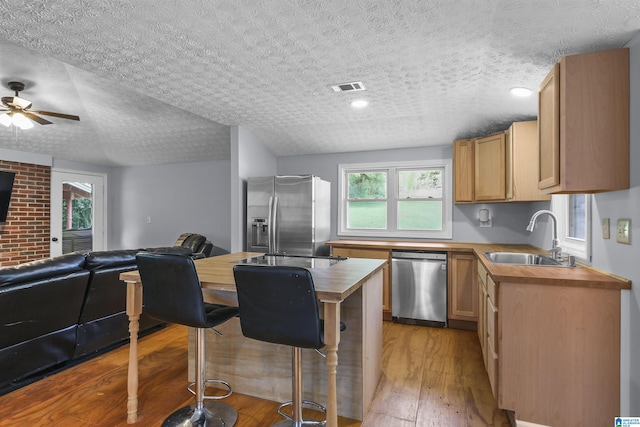 kitchen with appliances with stainless steel finishes, butcher block countertops, sink, light hardwood / wood-style floors, and a textured ceiling