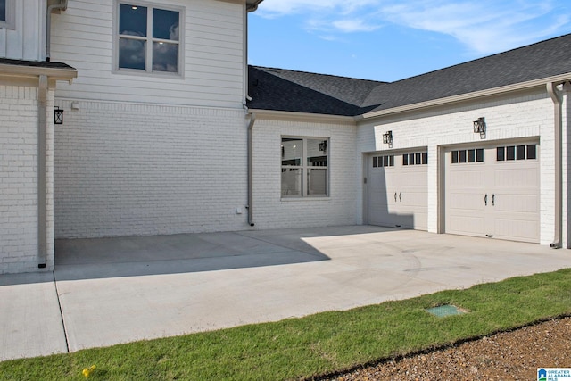 view of side of property with concrete driveway, brick siding, an attached garage, and roof with shingles