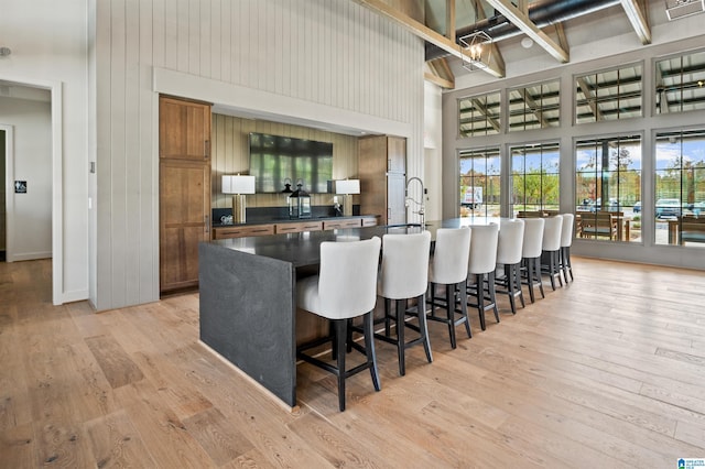 kitchen with light wood finished floors, brown cabinetry, dark countertops, a high ceiling, and a kitchen bar