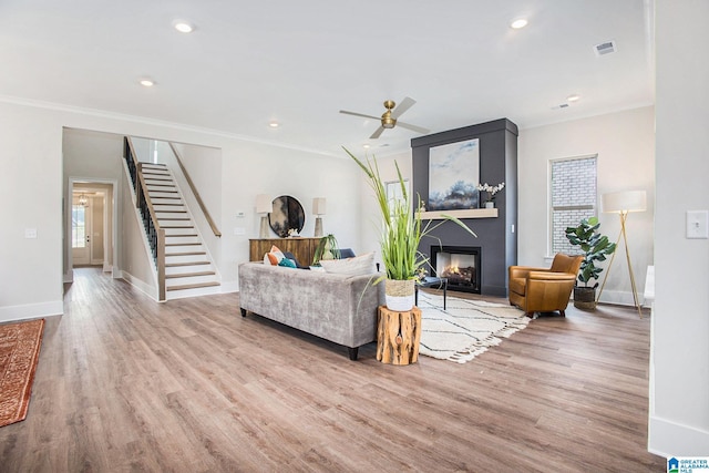 living area with a fireplace, visible vents, light wood-style floors, stairway, and crown molding