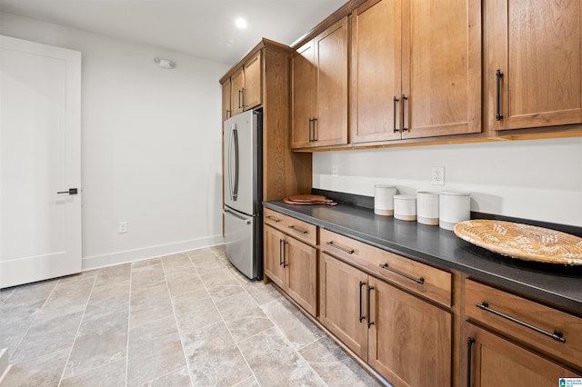 kitchen featuring baseboards, brown cabinetry, dark countertops, freestanding refrigerator, and recessed lighting