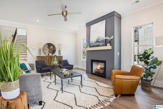 living room with light wood finished floors, baseboards, visible vents, a glass covered fireplace, and ornamental molding