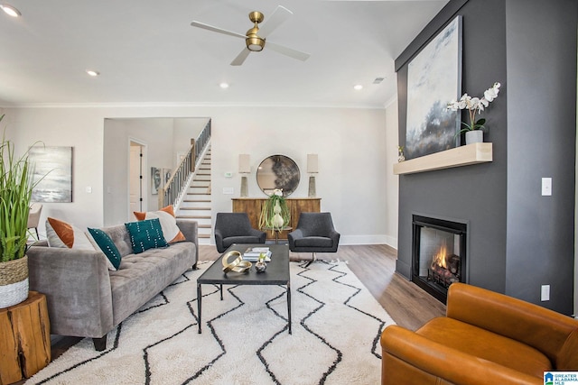 living area featuring crown molding, a fireplace, light wood-style flooring, baseboards, and stairs