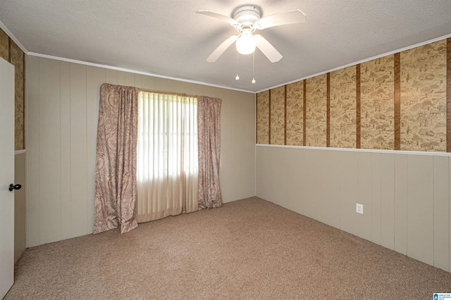 carpeted empty room featuring ceiling fan, wood walls, crown molding, and a textured ceiling