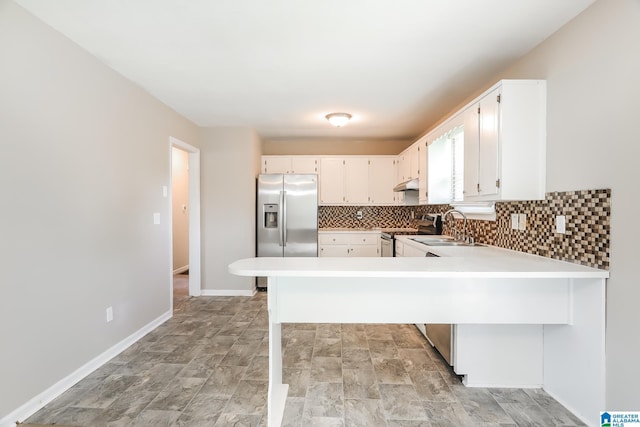 kitchen with kitchen peninsula, appliances with stainless steel finishes, decorative backsplash, sink, and white cabinets