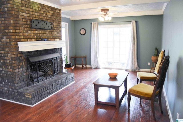 living area with dark wood-style flooring, a fireplace, ornamental molding, a ceiling fan, and baseboards