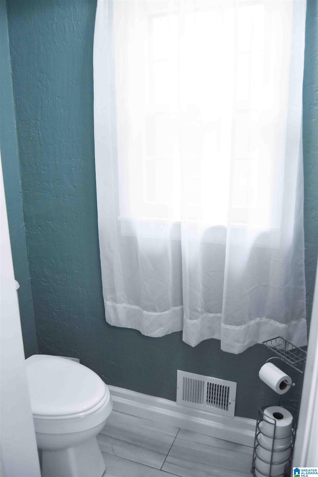 bathroom with visible vents, a textured wall, and toilet