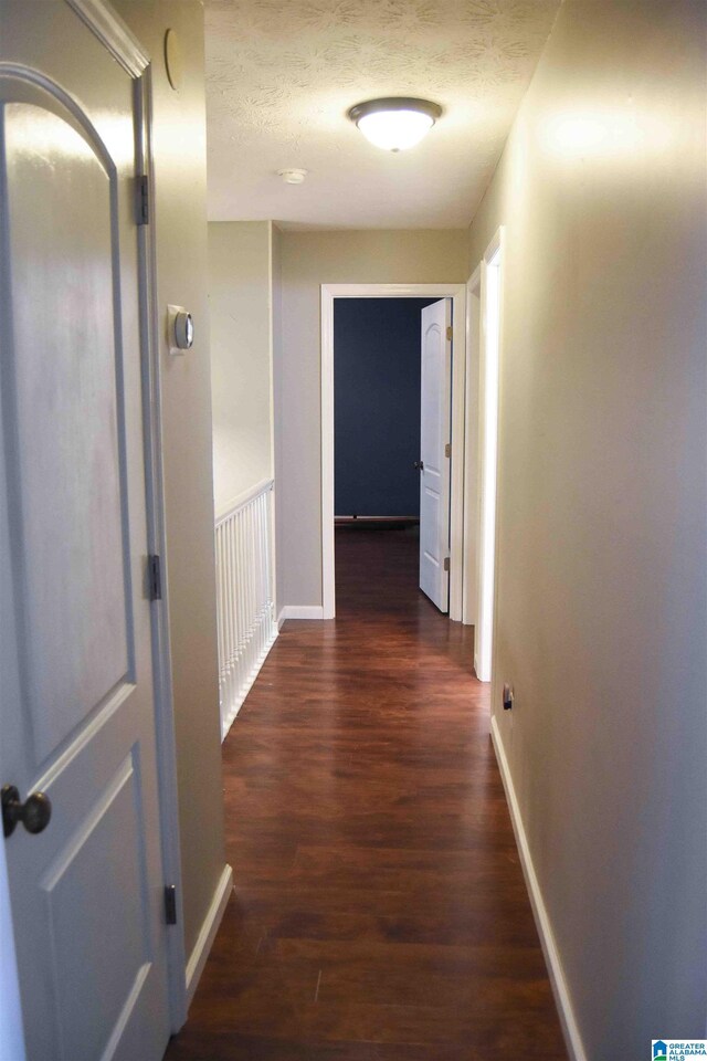 hall featuring dark wood finished floors, a textured ceiling, and baseboards