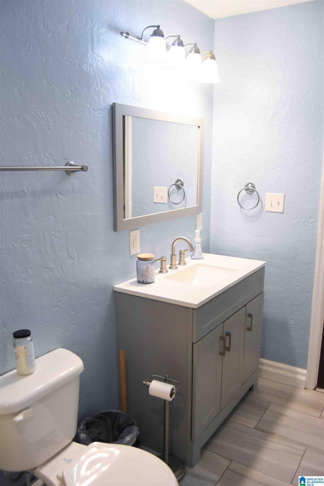 half bath featuring a textured wall, vanity, and toilet