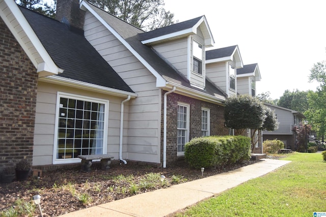 view of property exterior featuring a yard, brick siding, a chimney, and a shingled roof