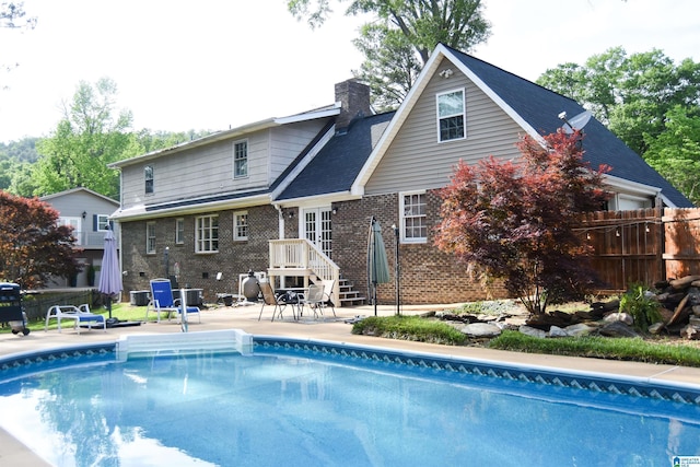 rear view of house featuring a fenced in pool, brick siding, a chimney, a patio area, and fence