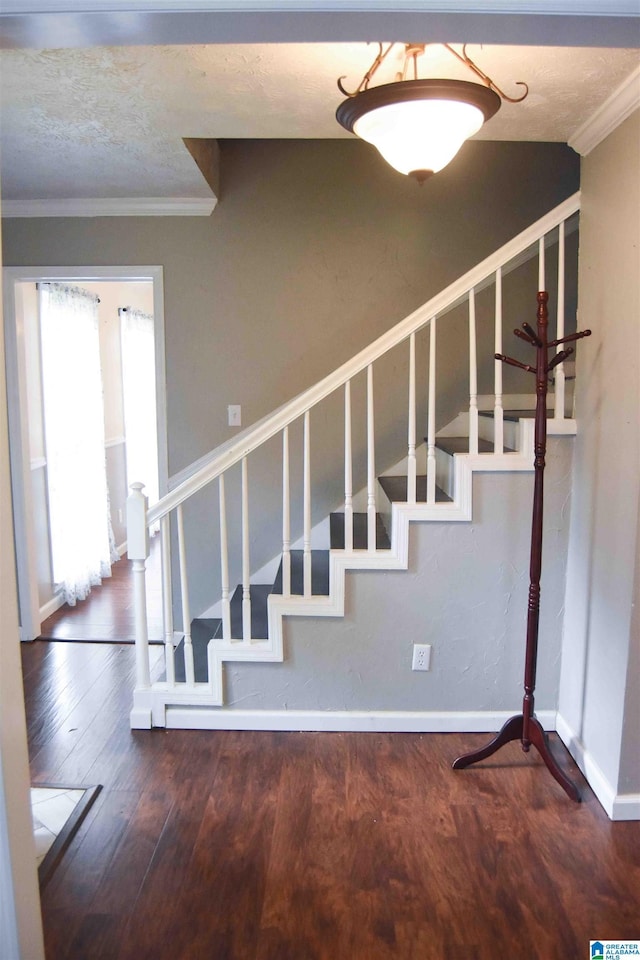 staircase featuring baseboards, a textured ceiling, wood finished floors, and crown molding