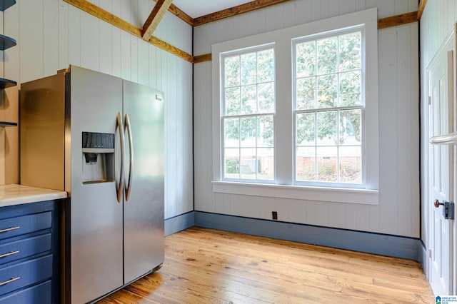 kitchen featuring wood walls, stainless steel fridge, light wood-type flooring, and a wealth of natural light