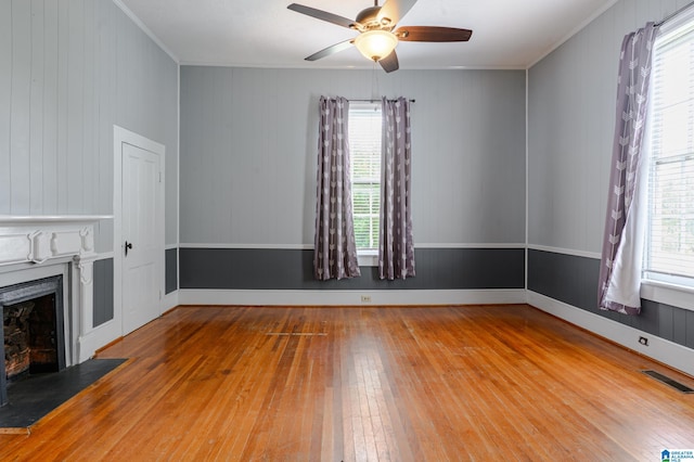 unfurnished living room with hardwood / wood-style flooring, ceiling fan, wood walls, and ornamental molding