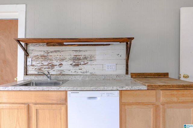 kitchen with light brown cabinetry, white dishwasher, wooden walls, and sink