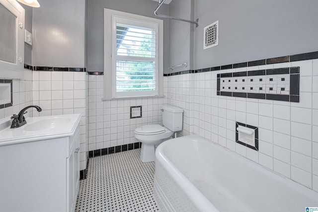 bathroom with vanity, tile walls, a bathtub, and toilet