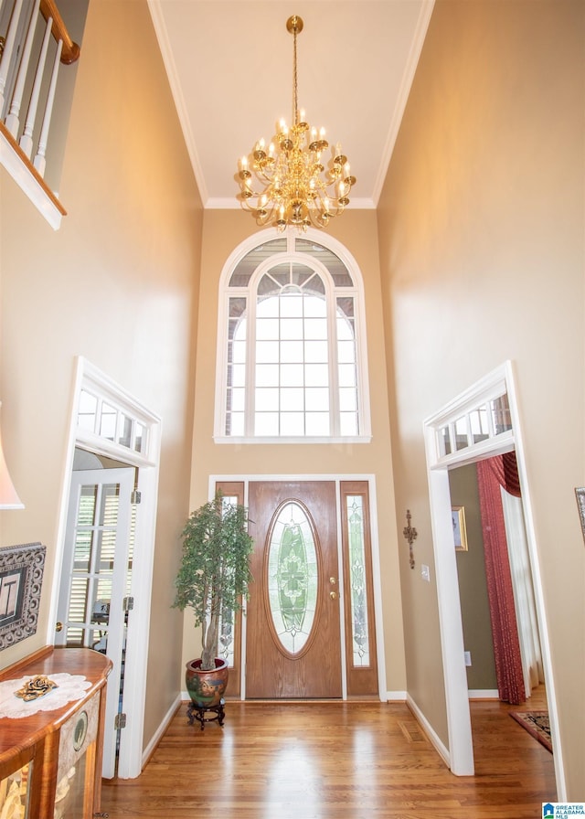 foyer entrance with light hardwood / wood-style floors, a towering ceiling, crown molding, and a chandelier