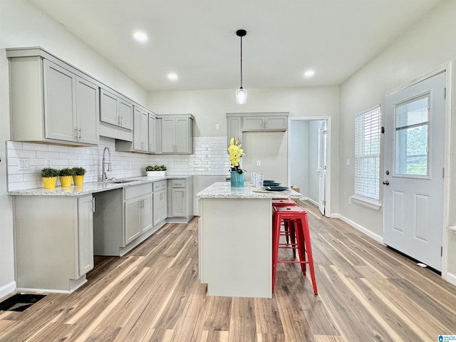 kitchen featuring light stone counters, sink, hardwood / wood-style floors, a center island, and gray cabinets