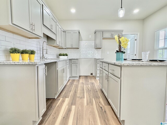 kitchen with tasteful backsplash, sink, decorative light fixtures, light hardwood / wood-style flooring, and gray cabinets