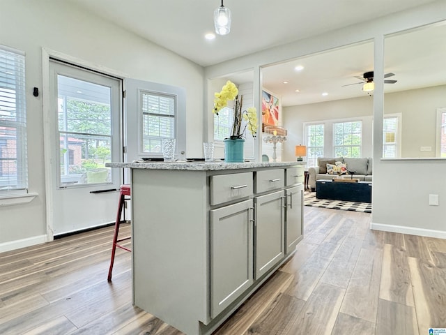 kitchen with light stone counters, light hardwood / wood-style floors, gray cabinets, a kitchen island, and hanging light fixtures