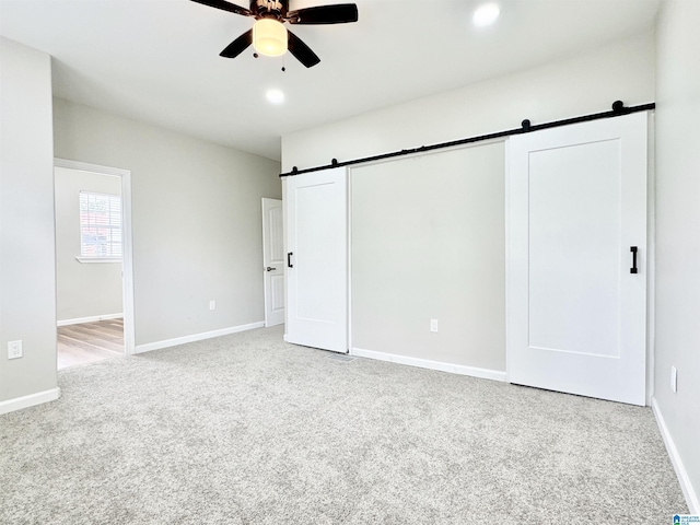 unfurnished bedroom featuring a barn door, light colored carpet, and ceiling fan