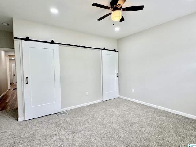 unfurnished bedroom featuring a barn door, ceiling fan, and carpet