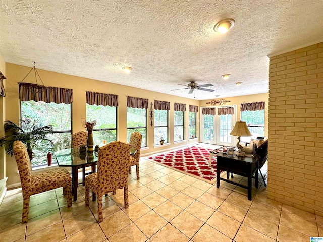 interior space with a textured ceiling, brick wall, light tile patterned floors, and ceiling fan