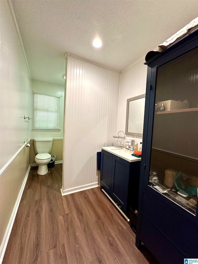 bathroom with crown molding, a textured ceiling, toilet, vanity, and wood-type flooring